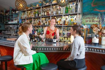 A bartender is pouring a glass of white wine for two people sitting at the bar at Ortega Fish Shack, a seafood restaurant in Wellington, New Zealand.