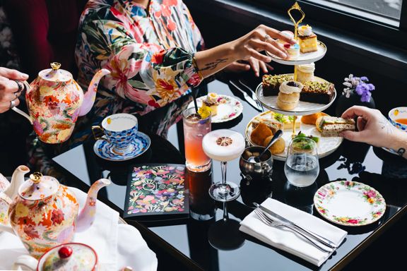 People enjoy high tea at QT Wellington. A three tiered plat, cocktails, and fancy teapots sit on the table.