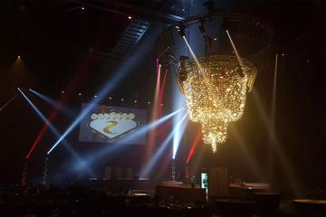 The interior of TSB Arena. The space is dark with white, red and yellow-ish spotlights and a huge circular chandelier suspended from rafters above.