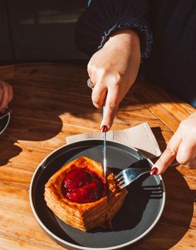A person uses a fork and knife to cut into a plum danish.