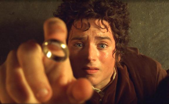 An iconic scene from the Lord of the Rings Film where Frodo Baggins is lying on the ground, reaching upward and the ring is falling onto his finger. 