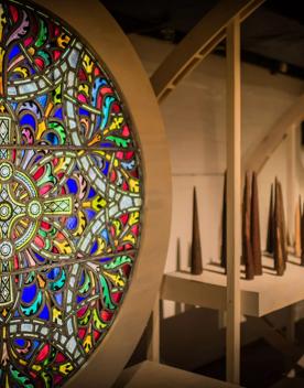 A circular stained glass with blue, yellow, red and green colours inside a gallery space in the Wellington Museum. 