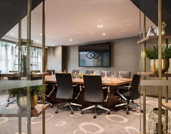 Boardroom table with twelve black leather seats around it. Large television screen on the wall.