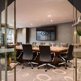 Boardroom table with twelve black leather seats around it. Large television screen on the wall.