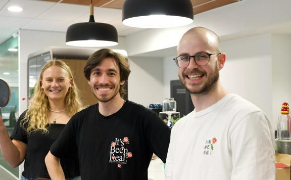 Three happy interns standing together in a modern office kitchen.