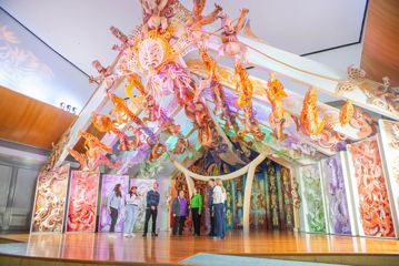 Eight people standing on stage below Rongomaraeroa - the marae at Te Papa which is covered in ornate colourful traditional maori carvings.