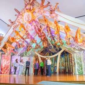 Eight people standing on stage below Rongomaraeroa - the marae at Te Papa which is covered in ornate colourful traditional maori carvings.