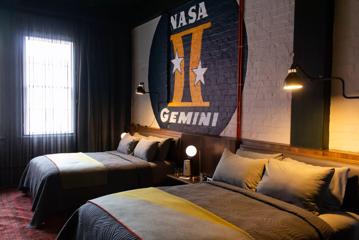 Inside a room in The Intrepid Hotel in Wellington, with two double beds and brick wall is painted with a large circle, inscribed with 'NASA' at the top and 'Gemini' at the bottom. The Gemini symbol, is centrally placed within the circle.