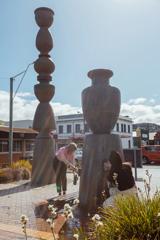 Two people fill bottles with water from Te Puna Wai Ora (Spring of Life) in Petone. Doubling as a sculpture, large concrete urns sit on top of each other.