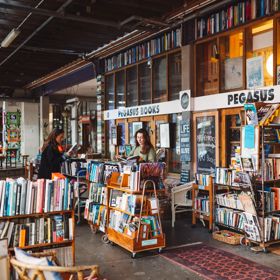 Two people browse through books outside Pegasus Books in Left Bank off Cuba Street. Pegasus Books is an older wooden building with shelves of eclectic books outside.
