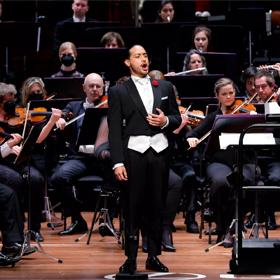 An opera singer is on stage surrounded by an orchestra during a performance.