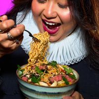 A close-up shows a person holding a bowl of noodles and lifting a forkful to eat, with greens and slices of meat visible in the dish.
