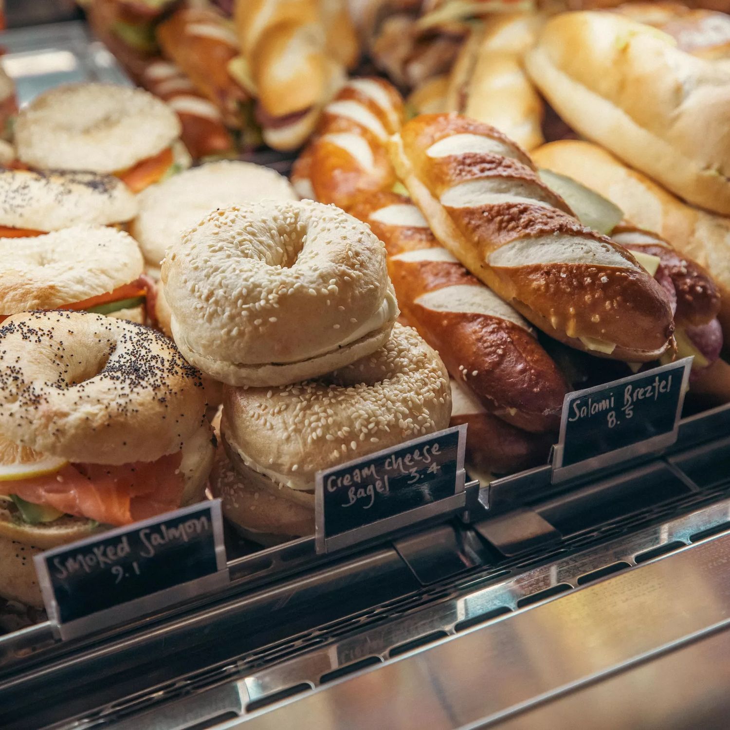 Assorted filled bagels, bread rolls and pastries displayed in a bakery cabinet.