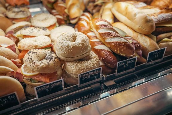 Assorted filled bagels, bread rolls and pastries displayed in a bakery cabinet.