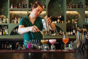 A bartender prepares cocktails behind the bar.