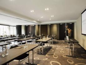 The Lady Norwood set up inside Sofitel for a business event, with 12 tables, each with 2 chairs, facing toward a projector.