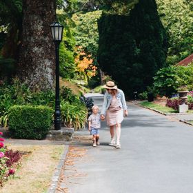 Mother and child walking down a concrete path surrounded by leafy trees and flowers.