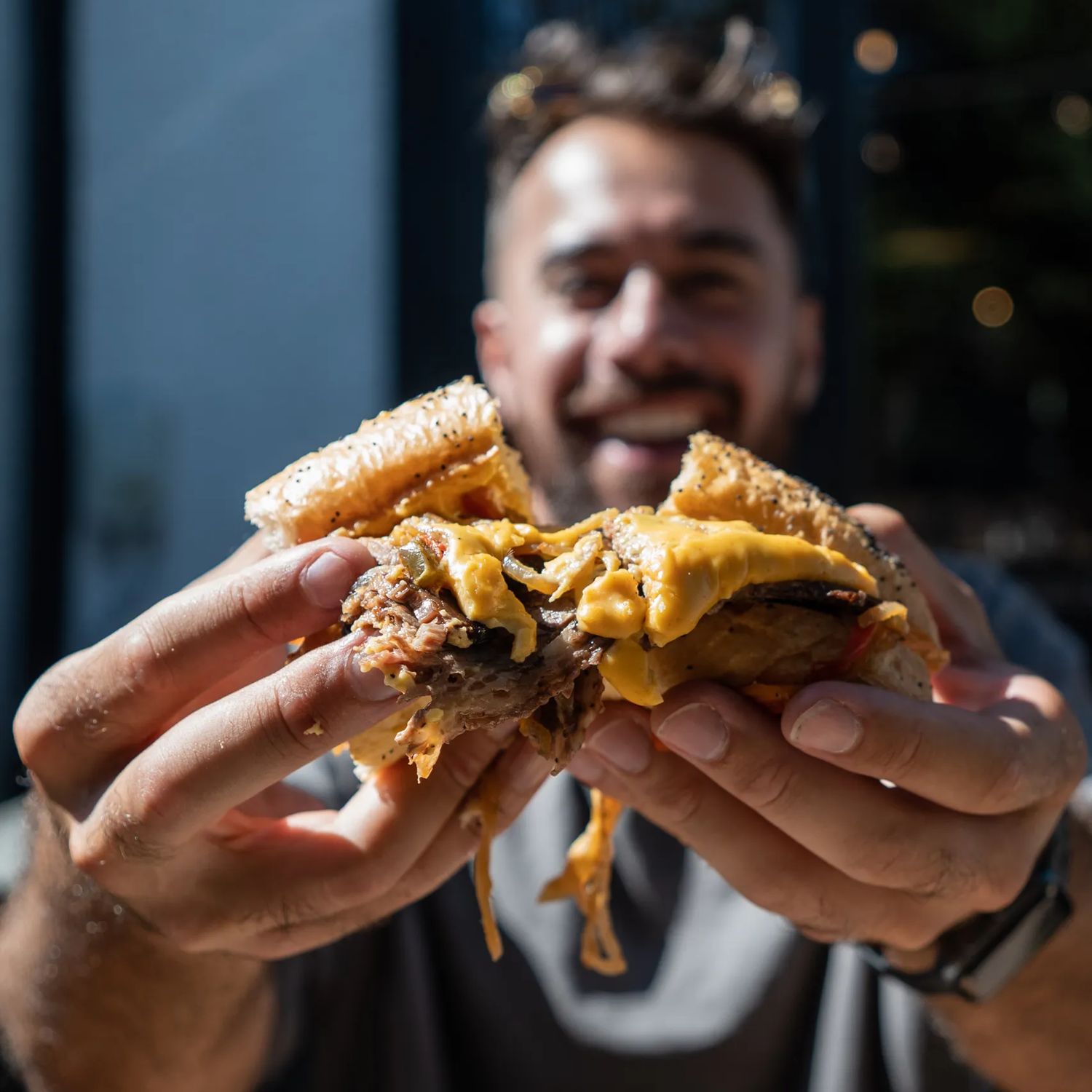 A person’s hands pull apart a burger with cheese oozing.