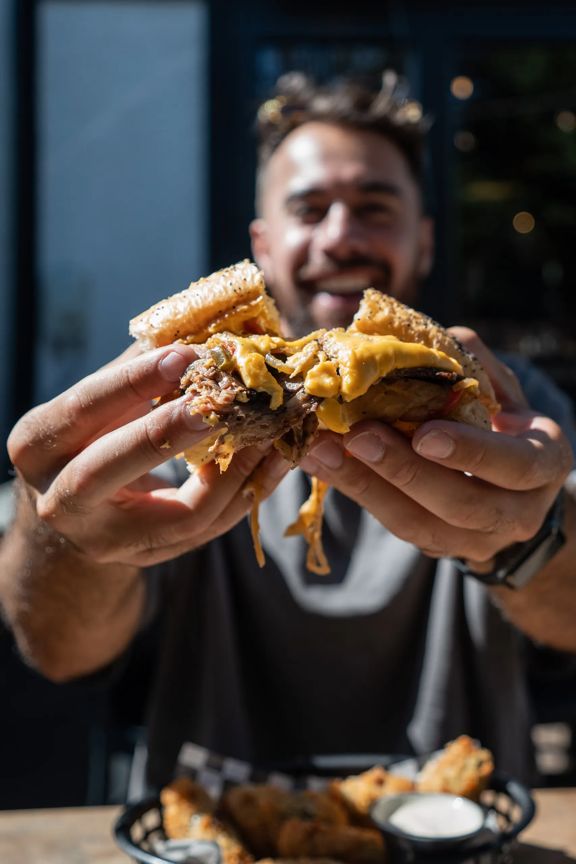 A person’s hands pull apart a burger with cheese oozing.