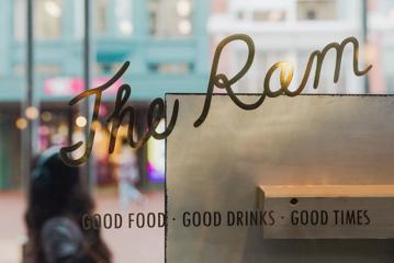 Looking through the glass window from the inside of The Ram, where a sign is printed on the glass - 'The ram, good Food, good drinks, good times.