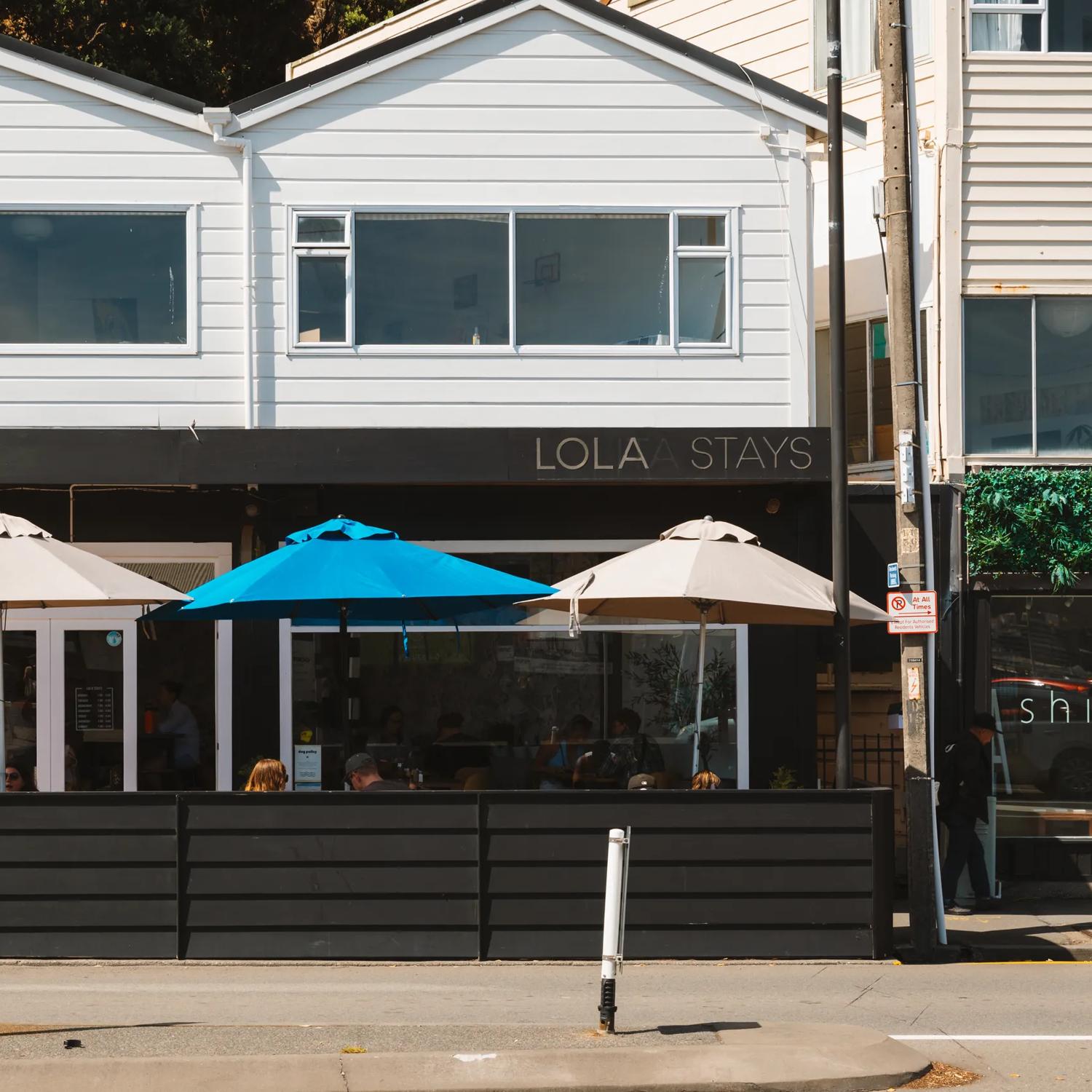 Outside Lola Stays, a café on Oriental Parade in the ground floor of a house. It has an outdoor eating area with umbrellas.