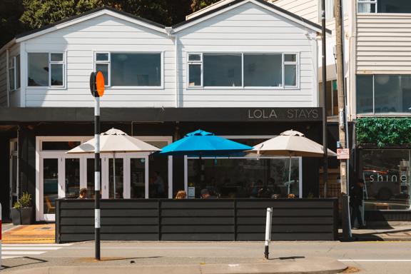 Outside Lola Stays, a café on Oriental Parade in the ground floor of a house. It has an outdoor eating area with umbrellas.