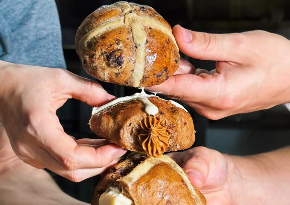 Three people's hands holding one hot cross bun each arranged vertically.