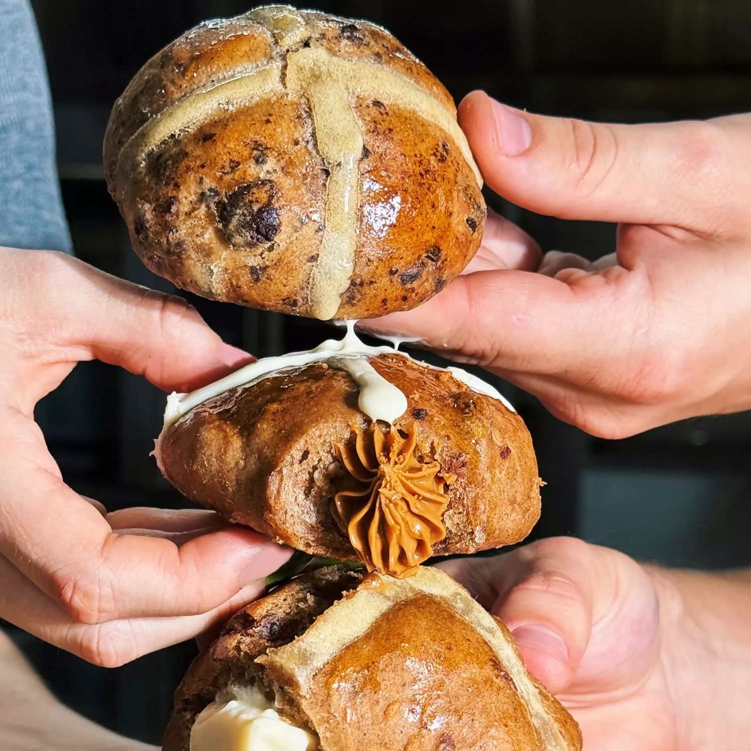 Three people's hands holding one hot cross bun each arranged vertically.