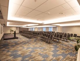 A conference room in the James Cook Hotel Gran Chancellor set up of a presentation. There are five rows of chairs and a small stage with a podium.