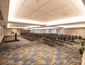 A conference room in the James Cook Hotel Gran Chancellor set up of a presentation. There are five rows of chairs and a small stage with a podium. 