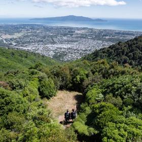 Two people sit on a bench in a small clearing at the summit of Hemi Matenga Scenic Reserve in the Kāpiti Coast.