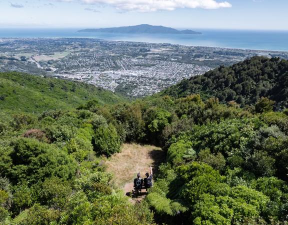 Two people sit on a bench in a small clearing at the summit of Hemi Matenga Scenic Reserve in the Kāpiti Coast.