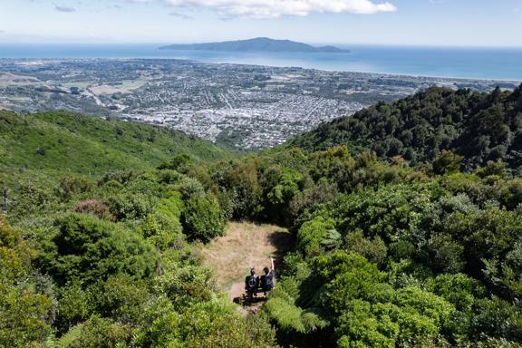 Two people sit on a bench in a small clearing at the summit of Hemi Matenga Scenic Reserve in the Kāpiti Coast.