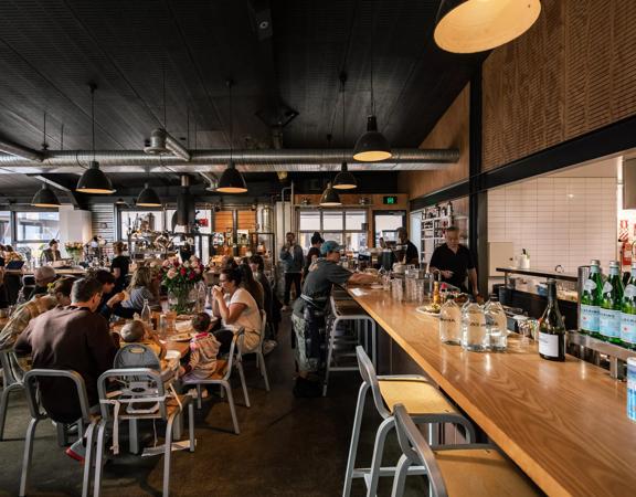 The interior of Prefab Eatery, a restaurant located on Jessie Street and Ebor Street in Te Aro Wellington, is filled with people enjoying food and drinks.