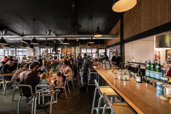 The interior of Prefab Eatery, a restaurant located on Jessie Street and Ebor Street in Te Aro Wellington, is filled with people enjoying food and drinks. 