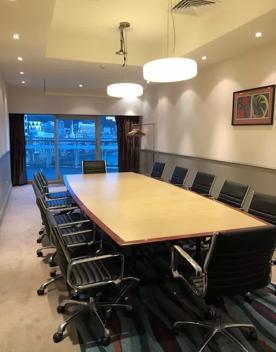 Inside the Copthorne Pencarrow Boardroom 1, a large wooden table with 12 seats sits in the middle of the room, with hanging lights and a floor to ceiling window.