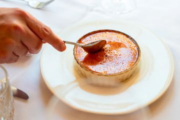 A silver spoon cracks the top of a perfect crème brûlée.