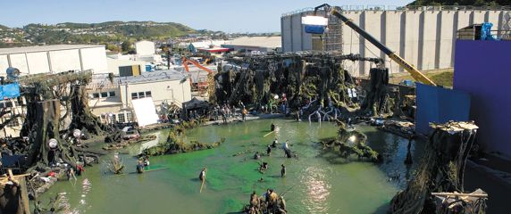 The backlot set at Stone Street Studios, where actors are wading through waist-deep green water resembling a swamp, and film crews are filming.