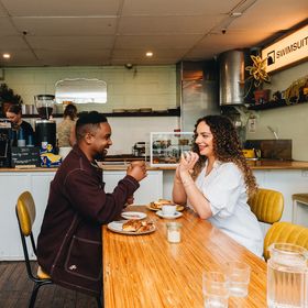 Two people sharing coffee and a meal inside Swimsuit on Dixon Street. The coffee counter is behind them with baristas working.