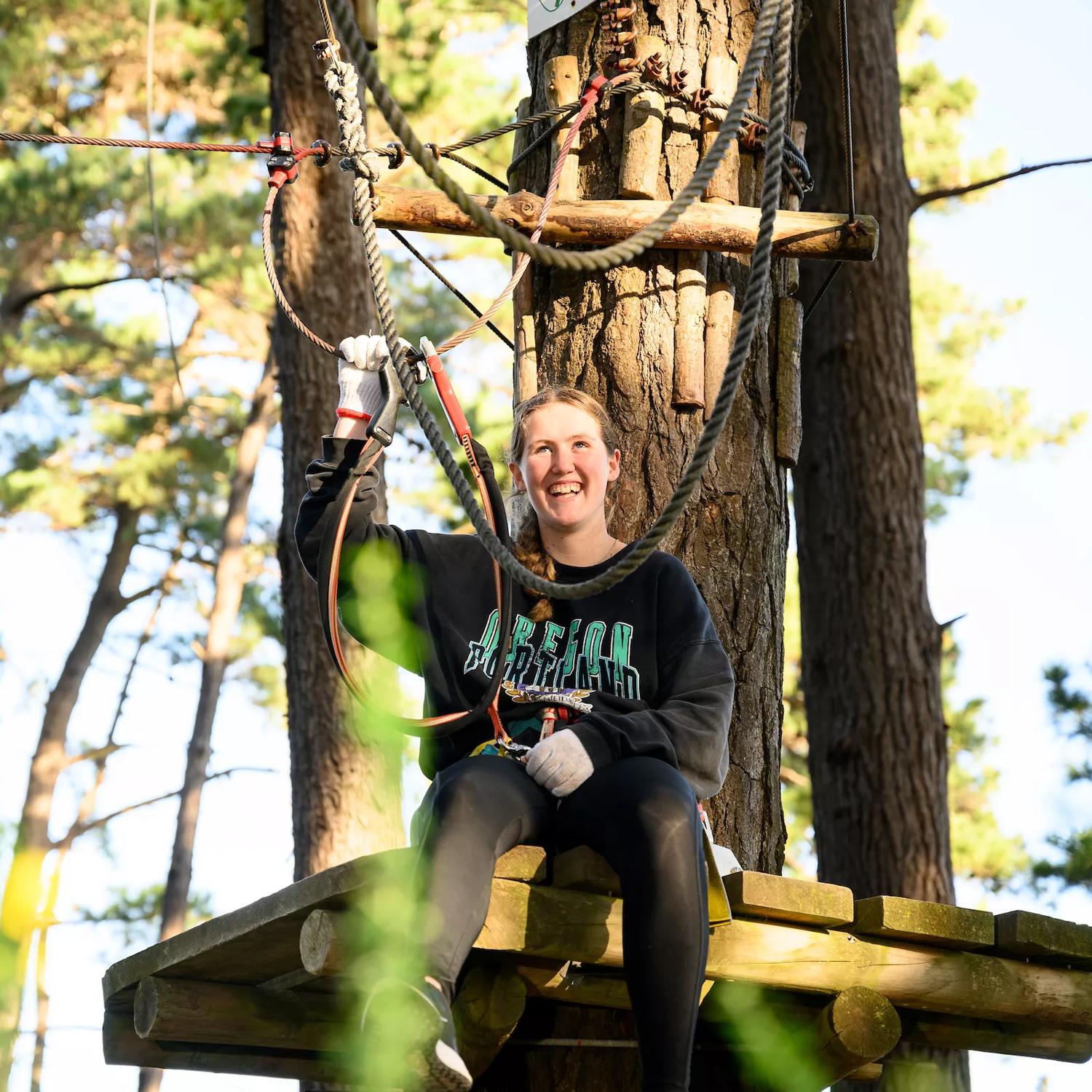 A person smiling while doing a top ropes course.