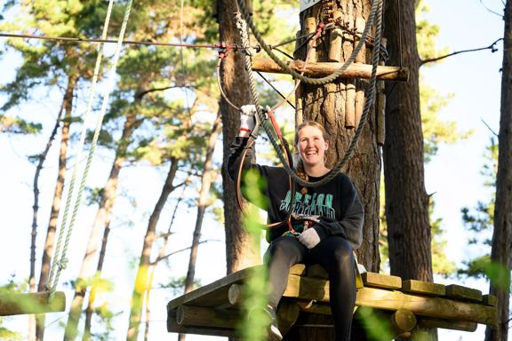 A person smiling while doing a top ropes course.