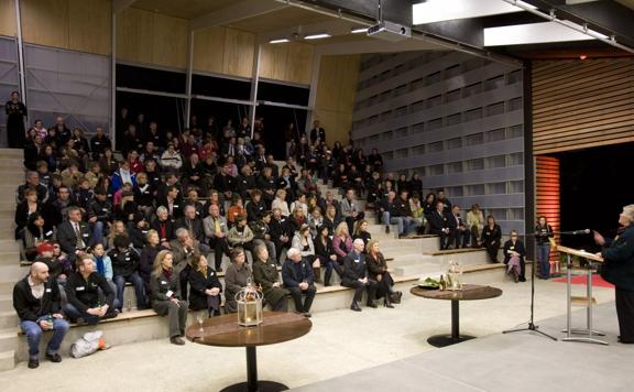 Inside the Wild Theatre at Wellington Zoo, concrete-tiered seating rises to the back wall. People fill the seats as a person stands at a lectern in front of them.