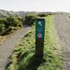 The top of the 4 degrees Track in Belmont Regional Park. A small signpost shows direction, with gravel paths cutting through farmland and hills in the background.