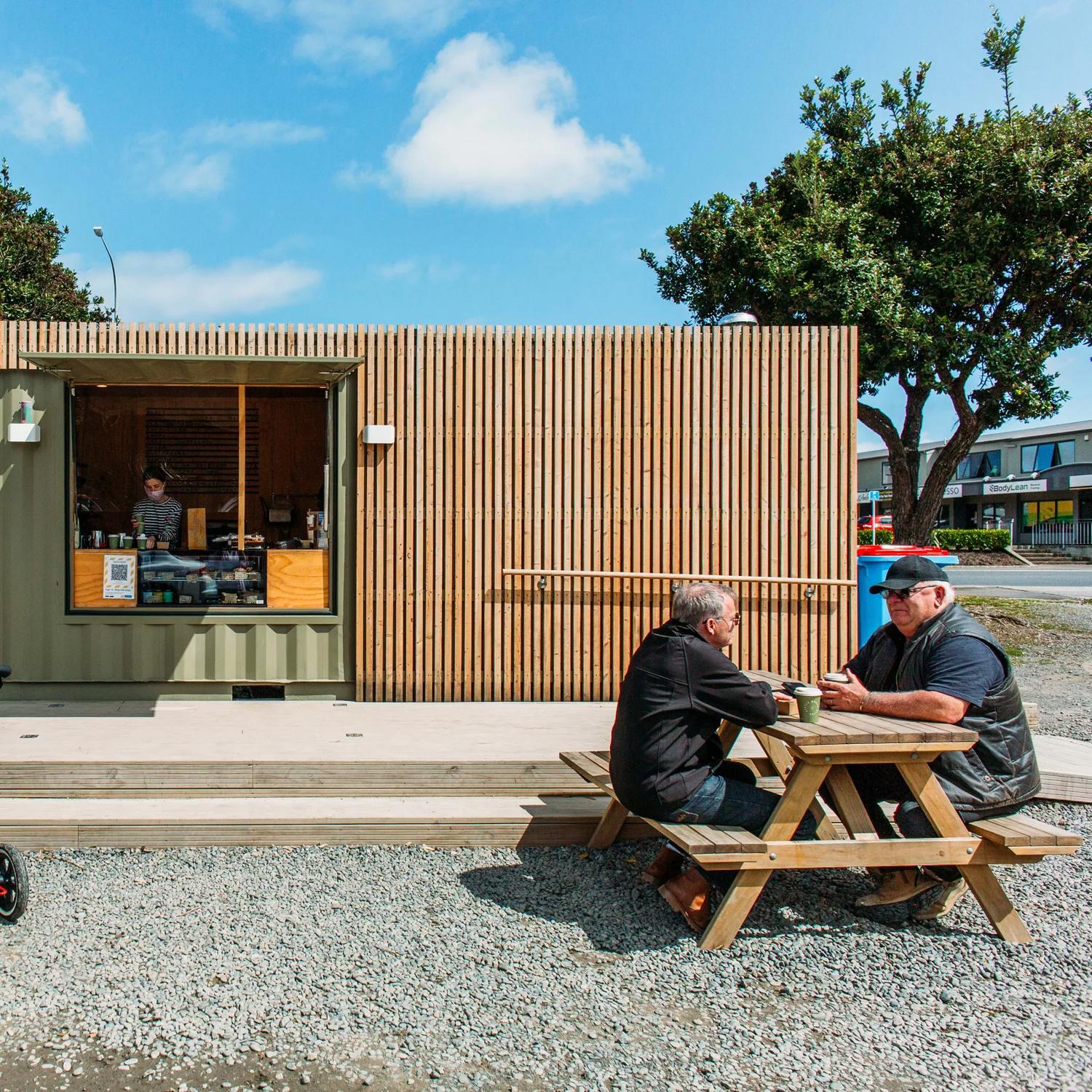Little Green Olive, a cafe in Porirua inside a green shipping container, with people eating on picnic tables outside.