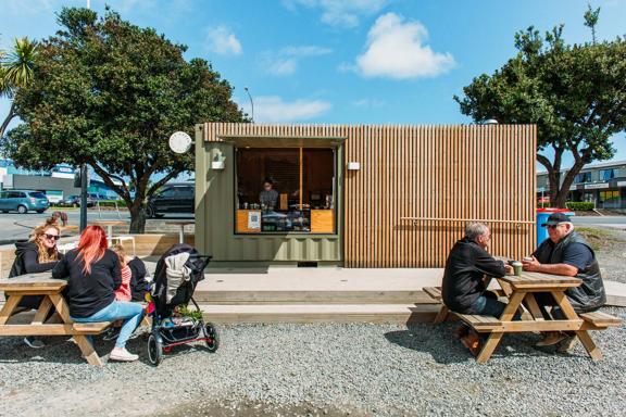 Little Green Olive, a cafe in Porirua inside a green shipping container, with people eating on picnic tables outside.