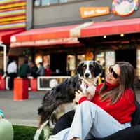 A person in a red sweater cuddles their dog sitting on a beanbag, on the grass at Glover Park, outside Rogue & Vagabond.