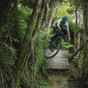 A downhill mountain bike rider going over a wooden drop jump on Dozer trail in Wainuiomata.