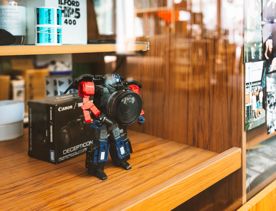 A transformer camera figurine on a wooden shelf behind a glass panel.