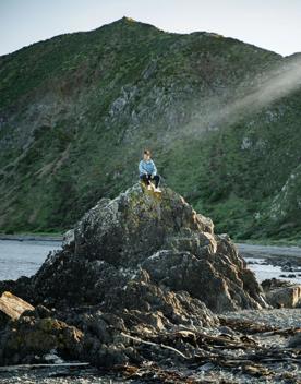 A person sits on top of a large rock on the Red Rock Coastal Walkway.