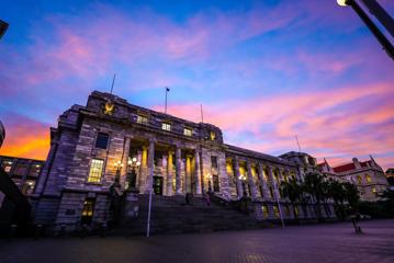 The exterior of the New Zealand Parliament building at 1 Museum Street, Pipitea in Wellington at sunset with pink-coloured clouds in the sky above.